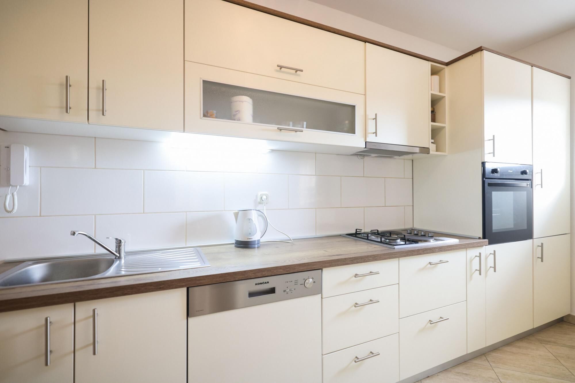 Una cucina moderna con mobili bianchi, lavello in acciaio inossidabile, lavastoviglie integrata, piano cottura a gas e forno a incasso.