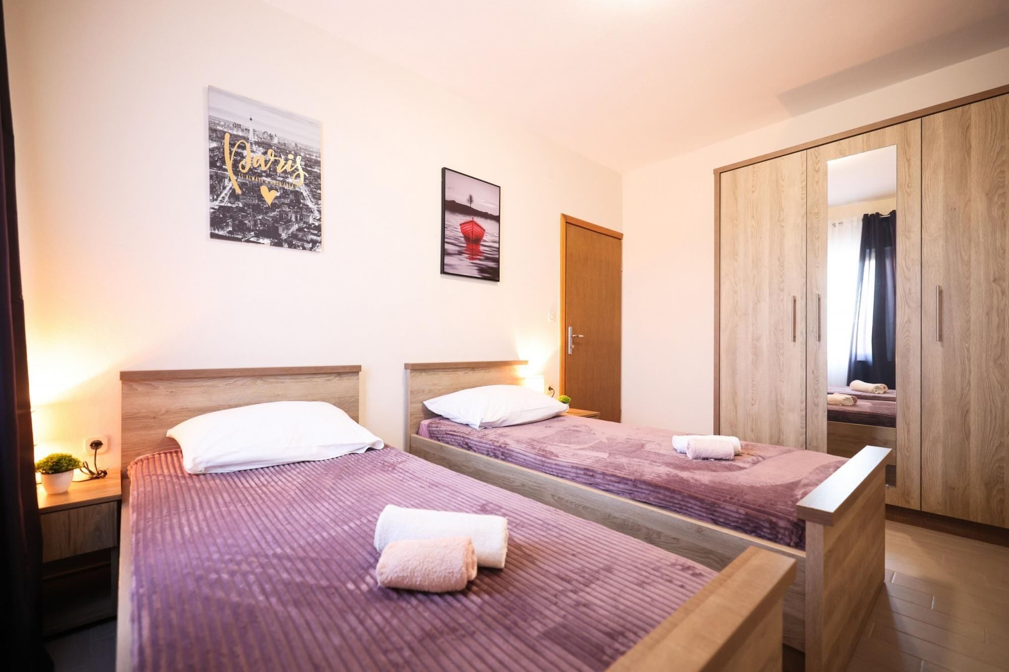A hotel room with two beds, a wardrobe, and a cityscape poster on the wall.