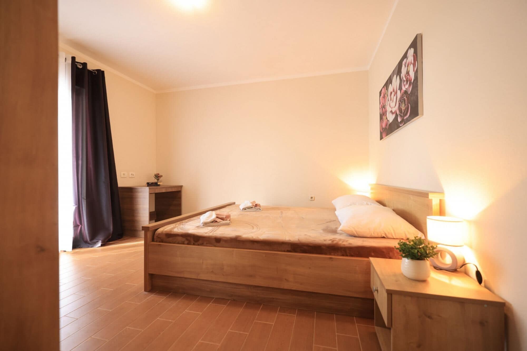 Une chambre à coucher avec un lit en bois, une table de chevet avec une lampe, une petite table de chevet avec une plante et un tableau accroché au mur.