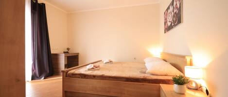 Une chambre à coucher avec un lit en bois, une table de chevet avec une lampe, une petite table de chevet avec une plante et un tableau accroché au mur.