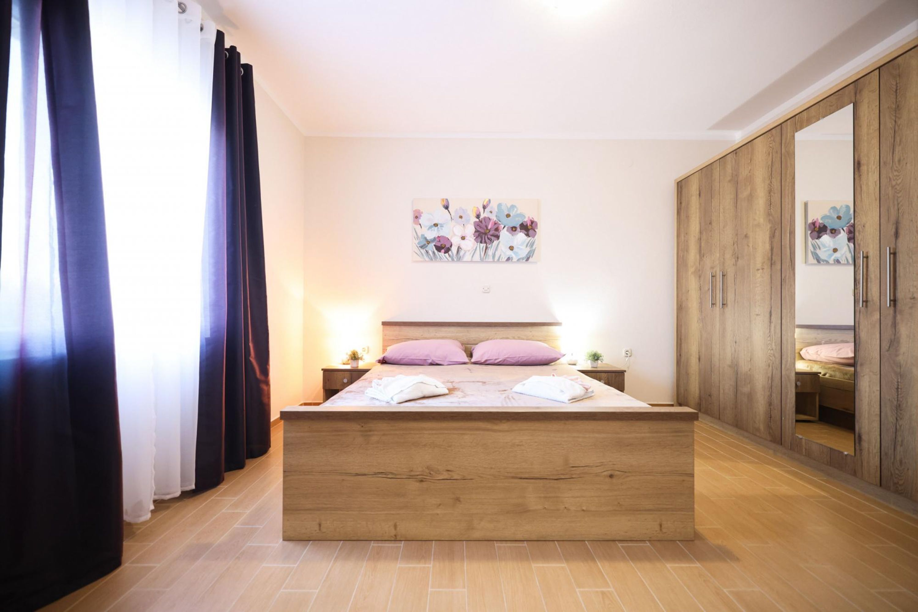 Una camera da letto con un letto in legno, un grande specchio e un quadro con motivi floreali al muro.