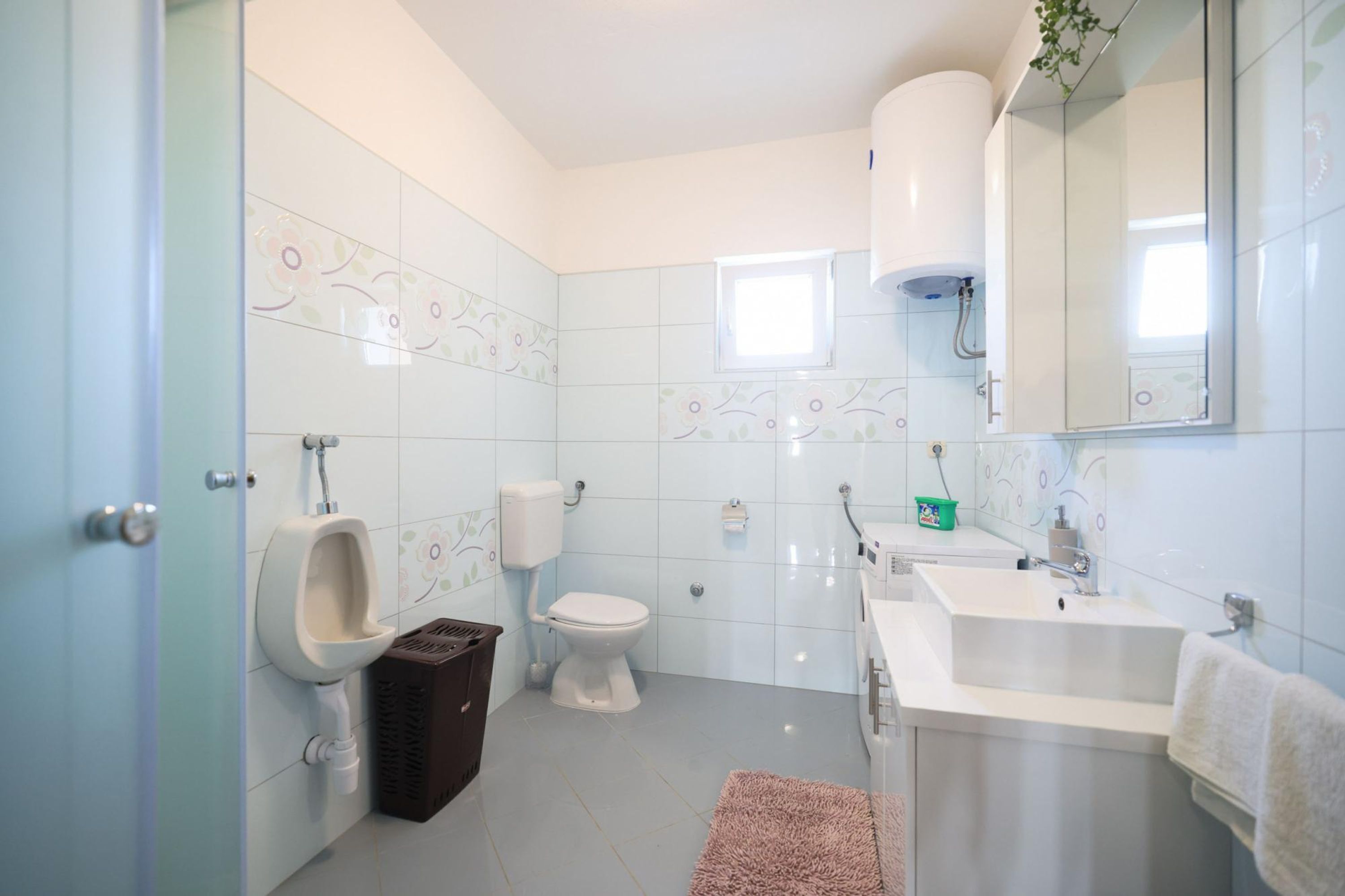 Un baño moderno con inodoro, orinal, lavamanos y espejo.