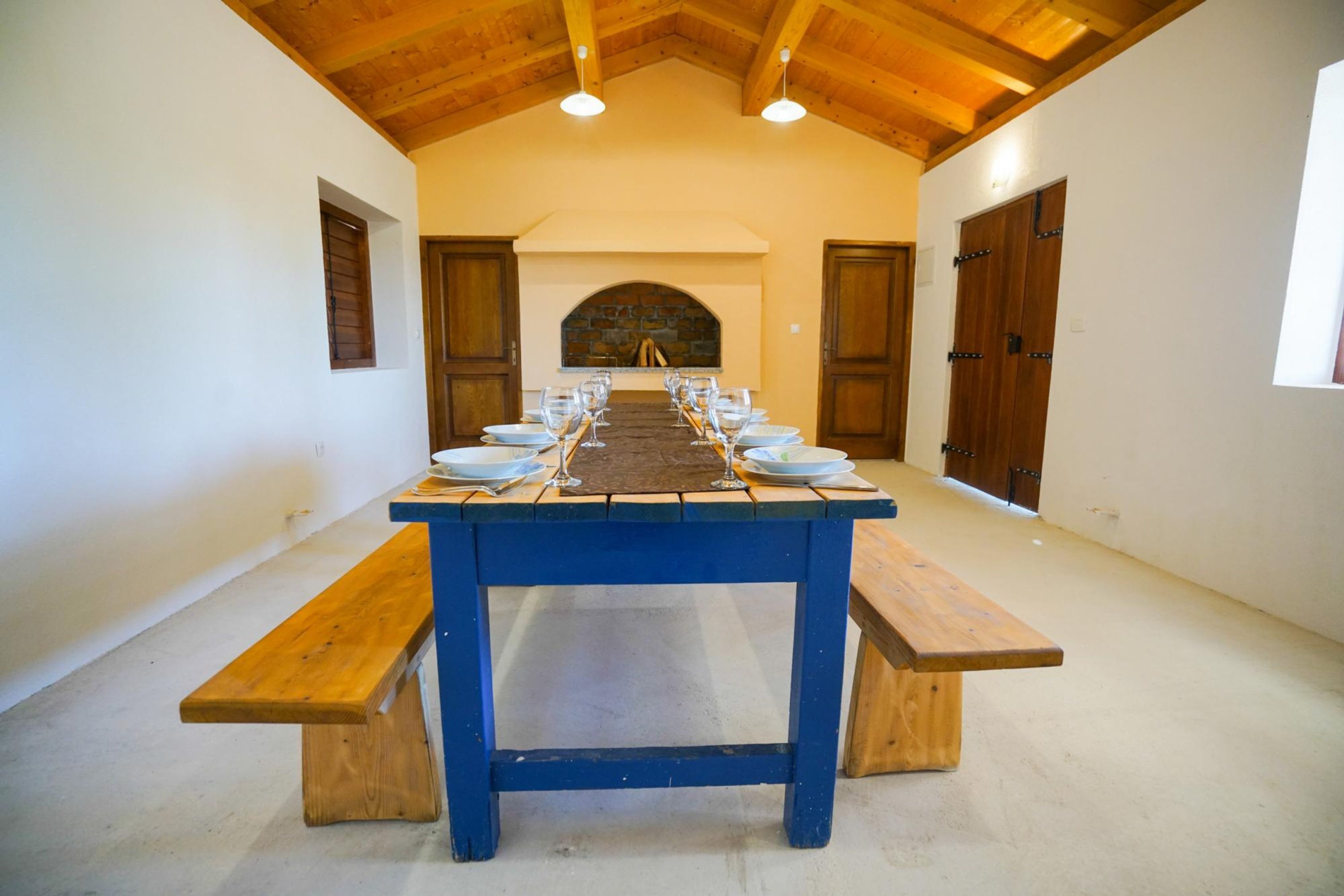 A long dining table with benches, a stone fireplace, and wooden doors.
