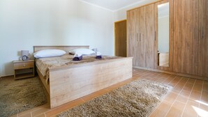 Une chambre à coucher avec un lit en bois, une table de chevet, une grande armoire et un sol recouvert d’une moquette.