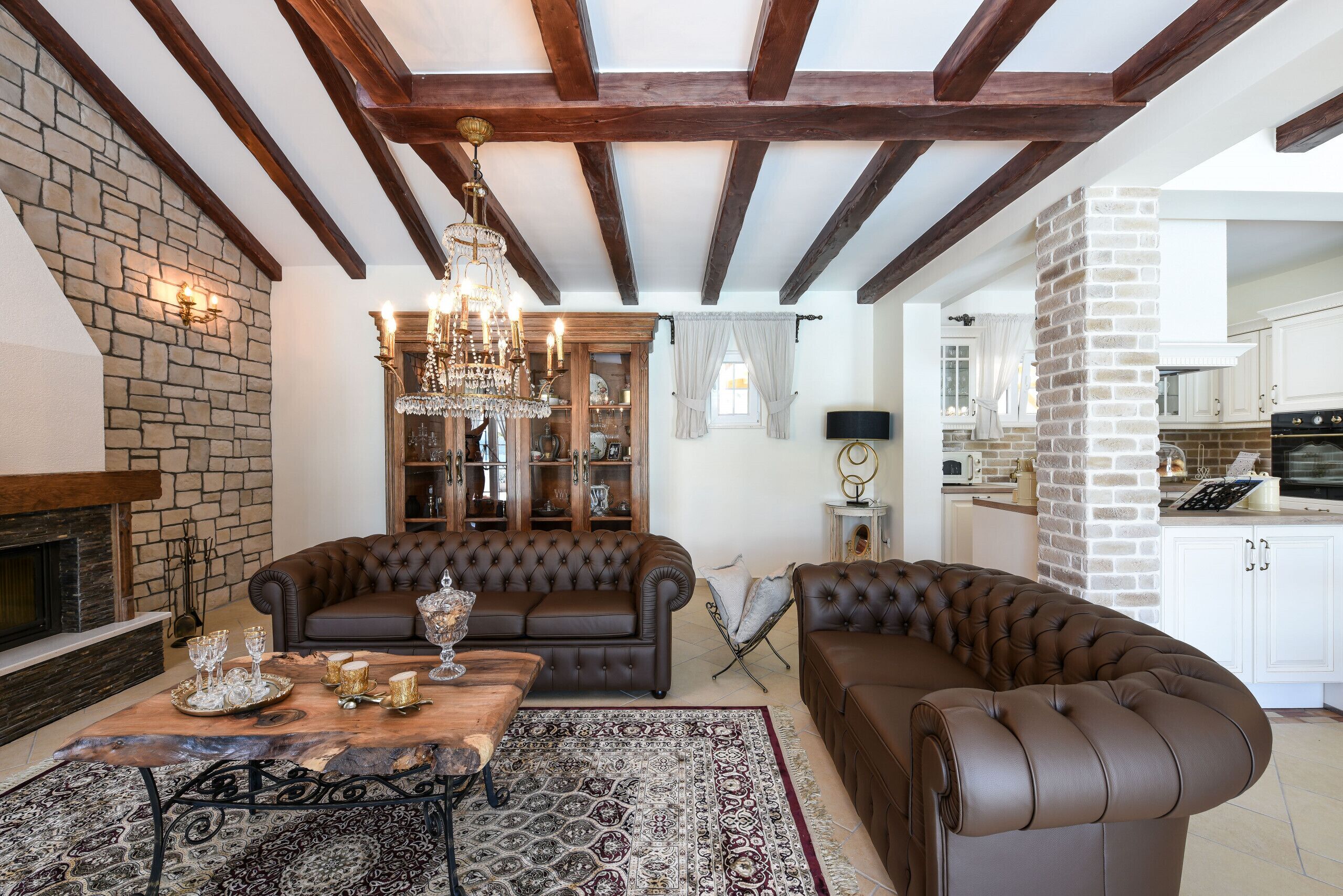 A cozy living room with a fireplace, leather sofas, a chandelier, and a stone wall.