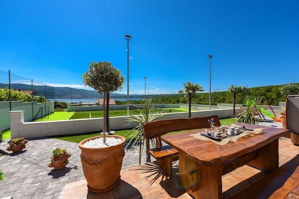 Une terrasse avec une table et des chaises en bois, entourée de plantes en pot et offrant une vue sur un paysage verdoyant.