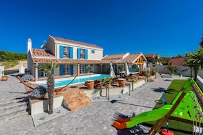 Une maison à deux étages avec une piscine, un espace salon extérieur et un coin jeux pour enfants.