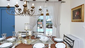 Ein Esszimmer mit Holztisch, gedecktem Tisch, einer Chandelierleuchtre und Blick ins Freie durch große Fenster.