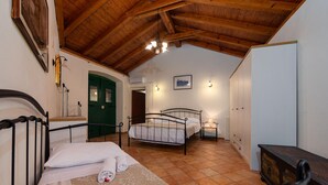 Une chambre avec un plafond en bois, un lit recouvert de draps blancs, une porte verte et un tableau blanc mural.