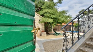 Une porte en bois peinte en vert, dotée d’une poignée en laiton, un escalier en pierre et une rampe en métal.