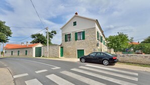 Un bâtiment en pierre avec des volets verts, une voiture garée devant et un passage piéton.