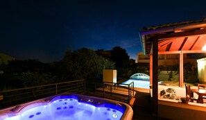 Relax in a serene hot tub under a shaded pergola, surrounded by a tranquil pool and lush trees.