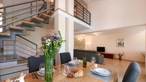 Ein Essbereich mit einem Holztisch, gedeckt für zwei Personen, einer Blumenvase und einer Treppe mit Geländer.