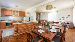 A modern kitchen with wooden cabinets, a dining area with a wooden table set for four, and a living room with a sofa and a coffee table. - Villa Pine Zadarvillas (Kukljica)