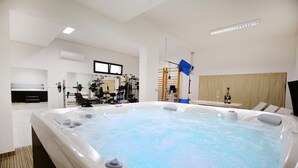 Une salle de spa moderne équipée d’un jacuzzi, d’appareils d’exercice et d’une table de massage en bois.