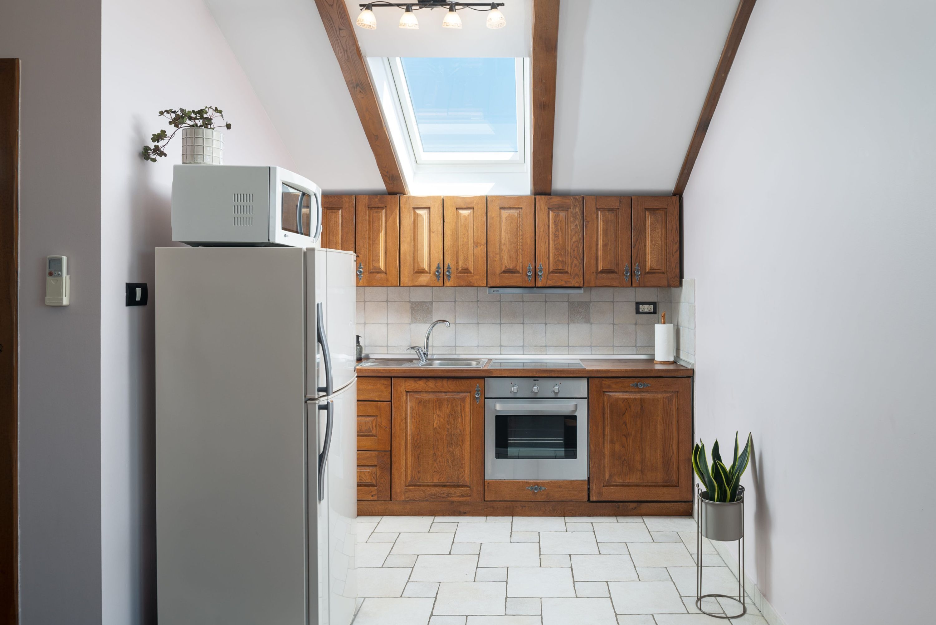 A kitchen with wooden cabinets, a white refrigerator, an oven, and a skylight.
