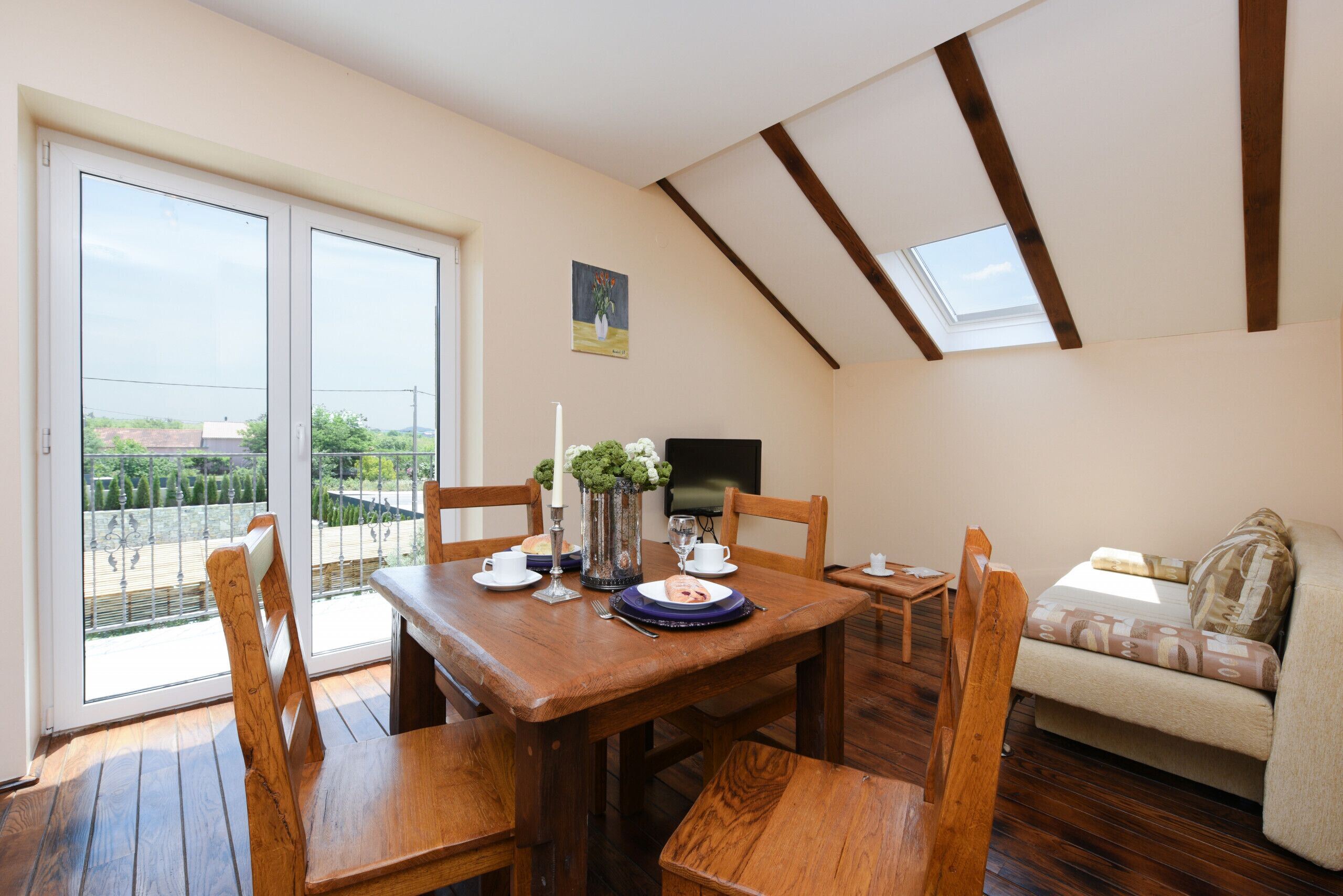 Zona pranzo con tavolo in legno, sedie e vista su un giardino esterno attraverso porte in vetro.