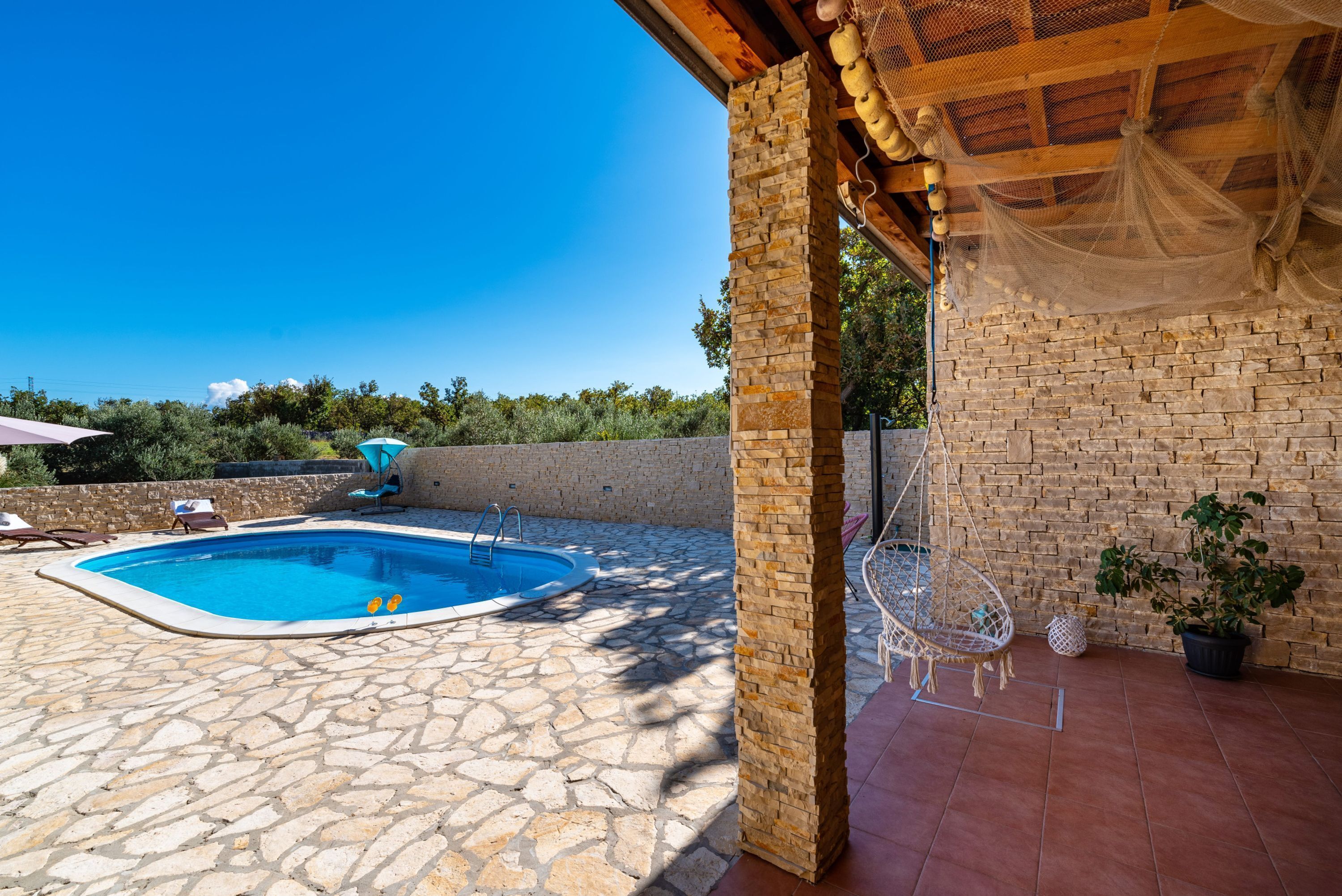 Una piscina de piedra, una silla colgante y una planta en maceta en un espacio exterior cubierto.