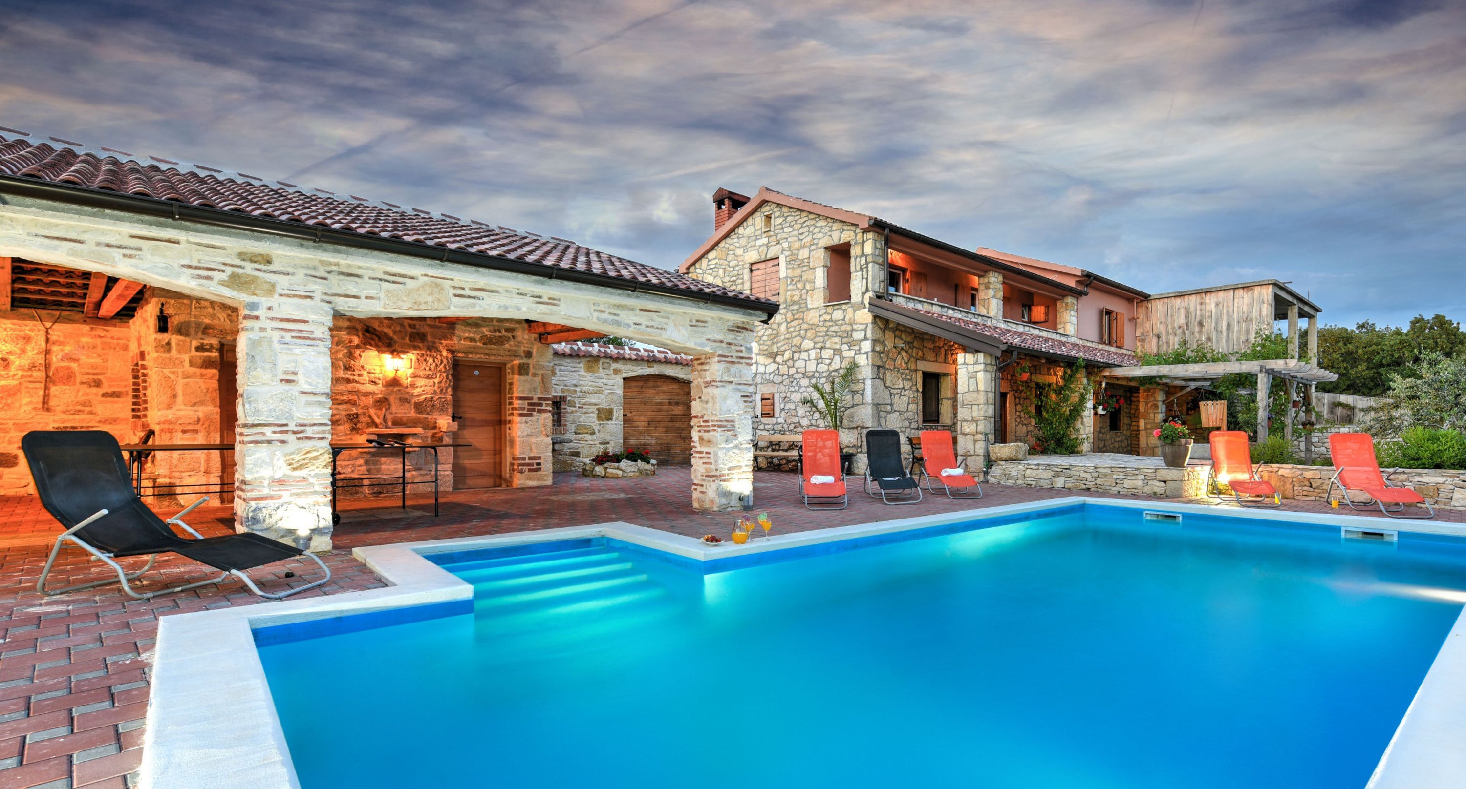 A pool area with stone buildings, outdoor seating, and a clear sky.