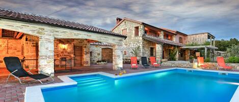 A pool area with stone buildings, outdoor seating, and a clear sky.