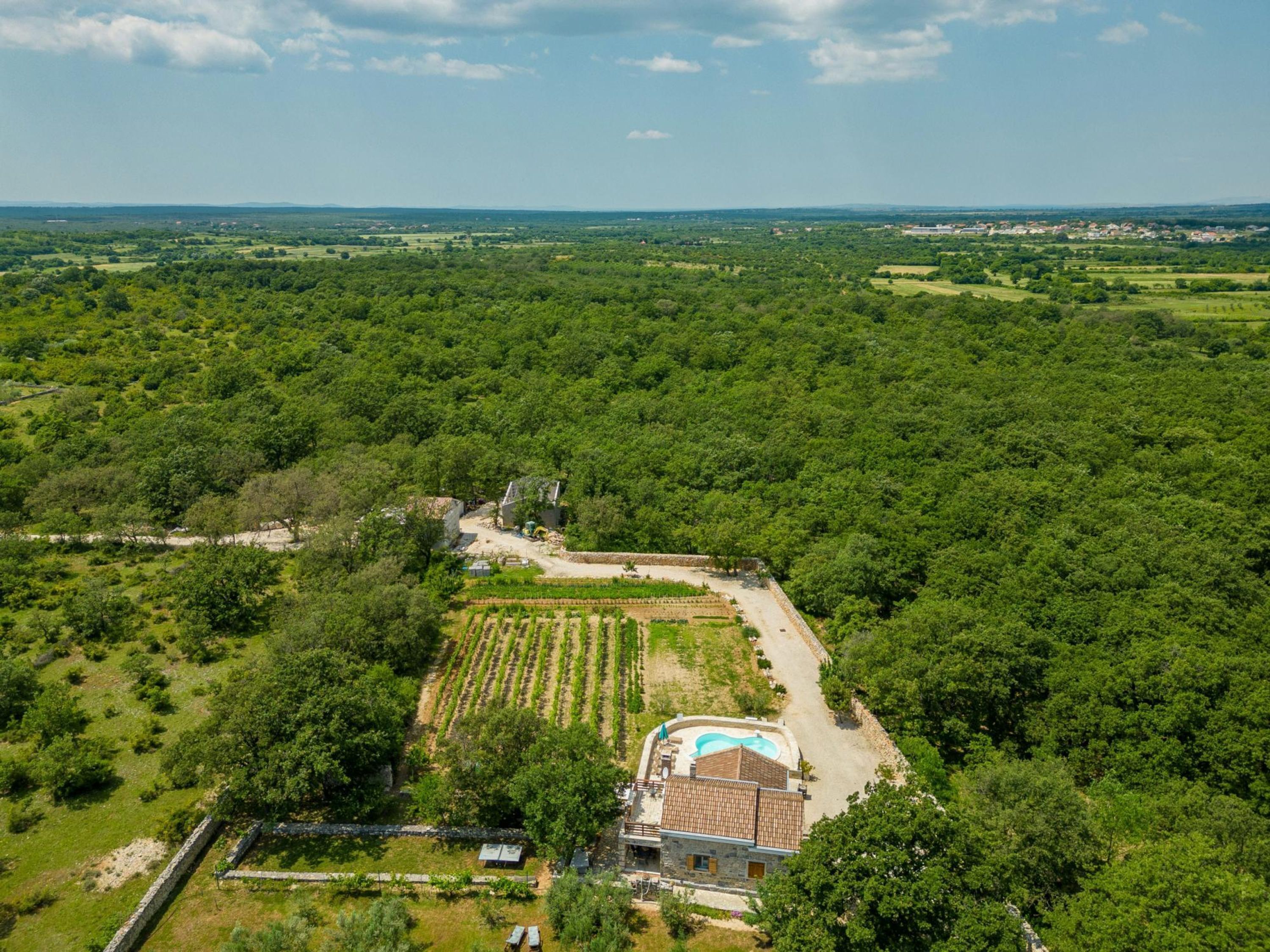 An aerial view of a property with a swimming pool, a stone building, and surrounding greenery.