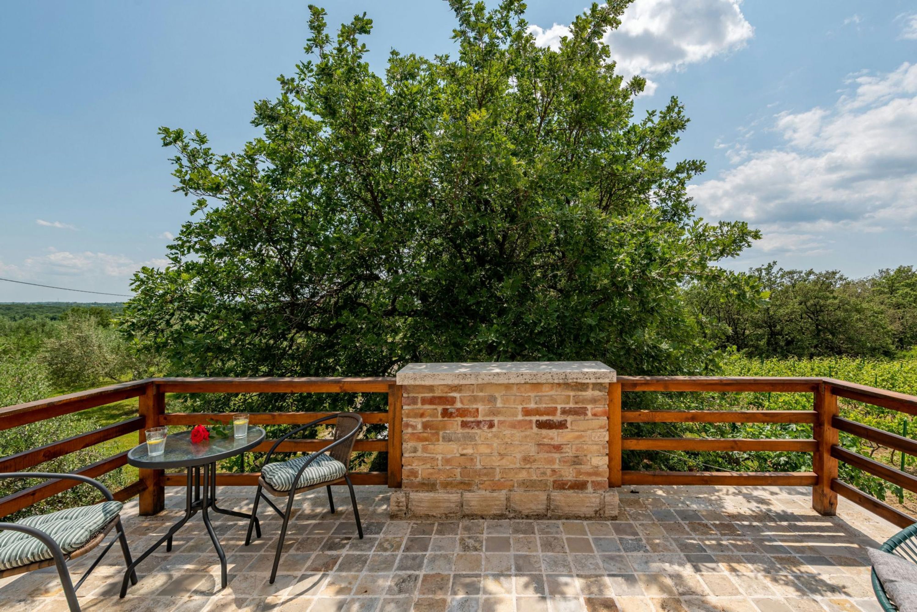An outdoor patio with a brick wall, a wooden railing, and a table with chairs.