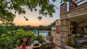 A patio with a stone table, a hanging chair, and a view of a swimming pool and trees. - Villa Rosemary Zadarvillas (Policnik)