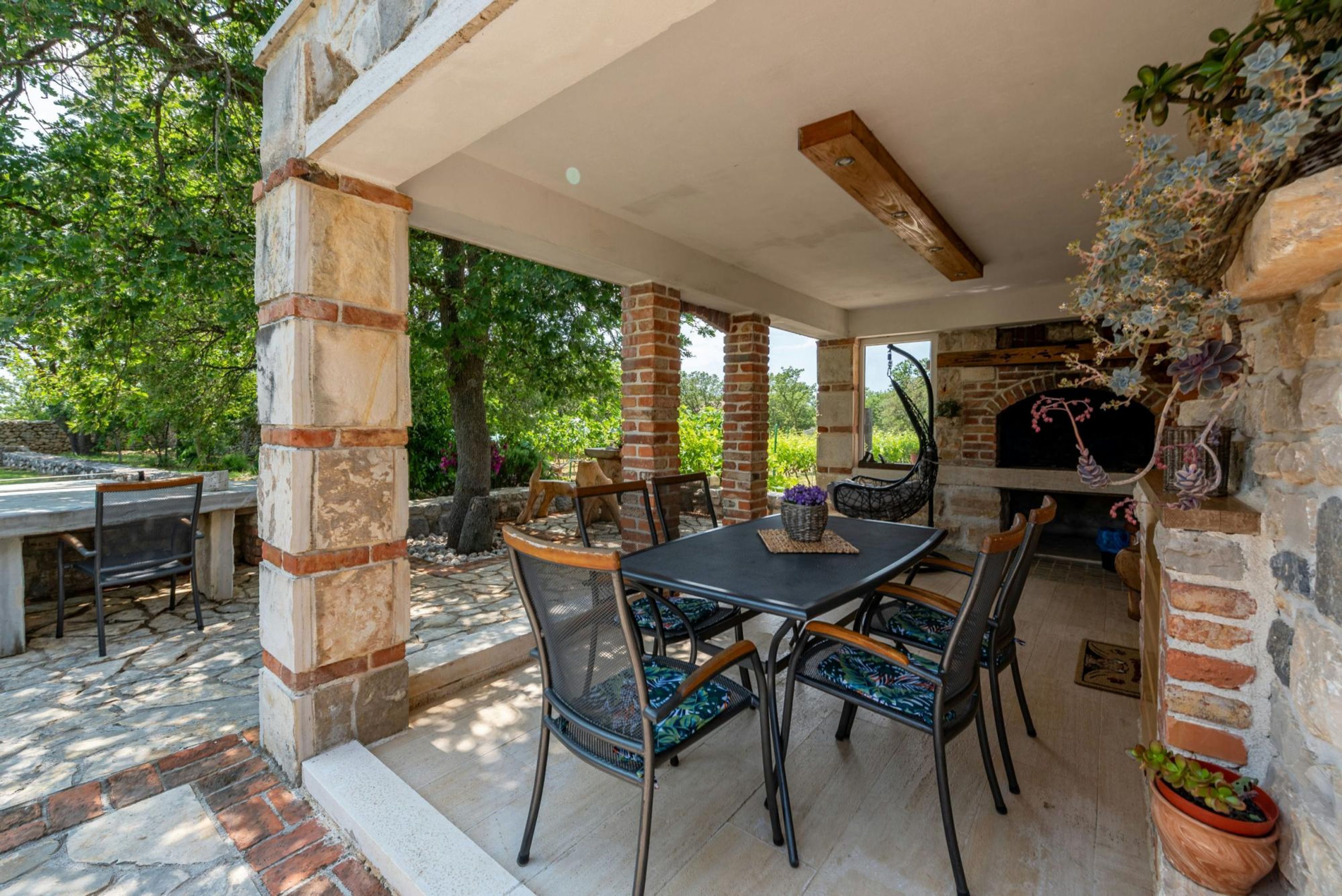 An outdoor patio with a brick fireplace, stone pillars, and a table with chairs.