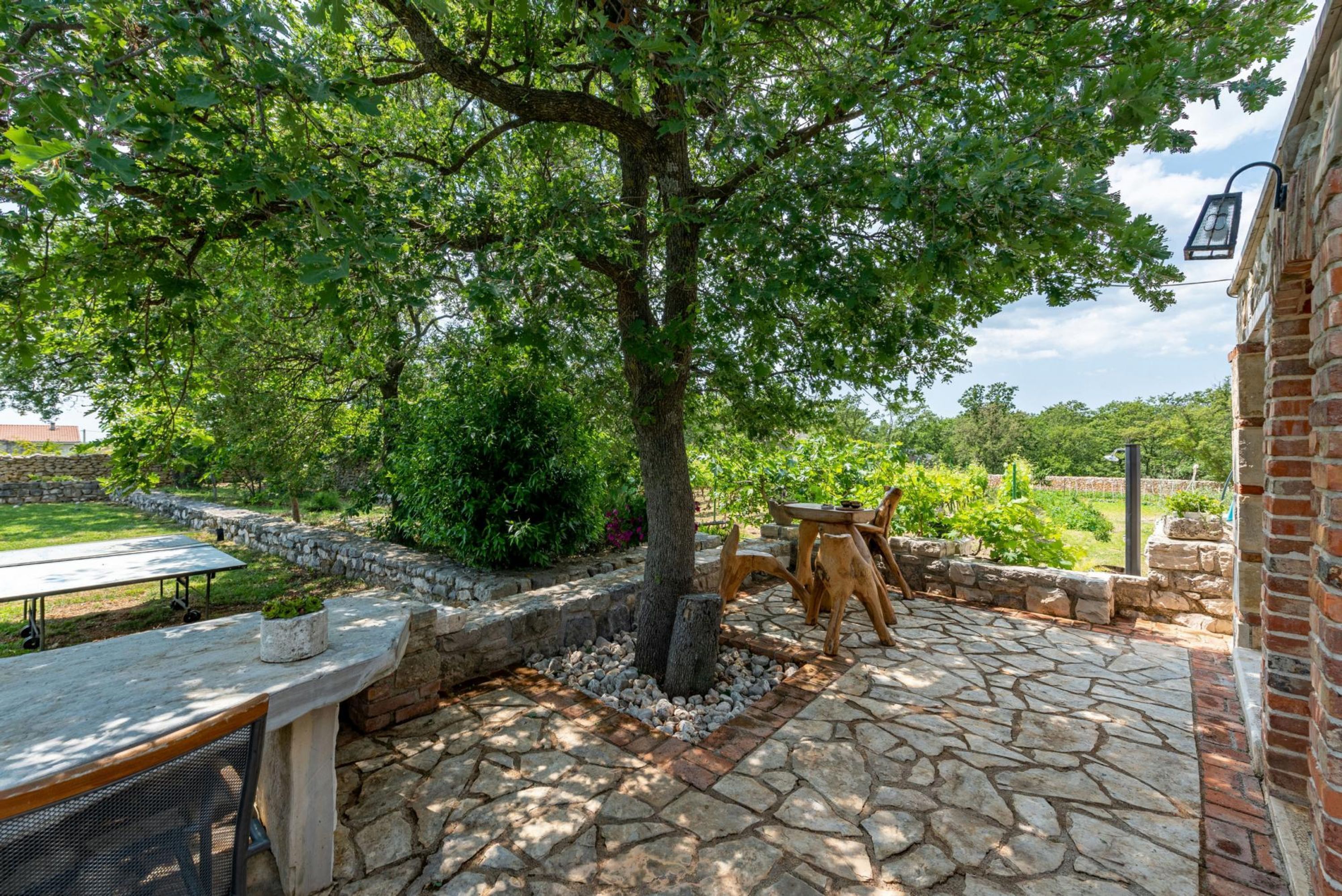 Un espace extérieur aménagé avec un sol en pierre, une table en bois et un banc pour s’asseoir.