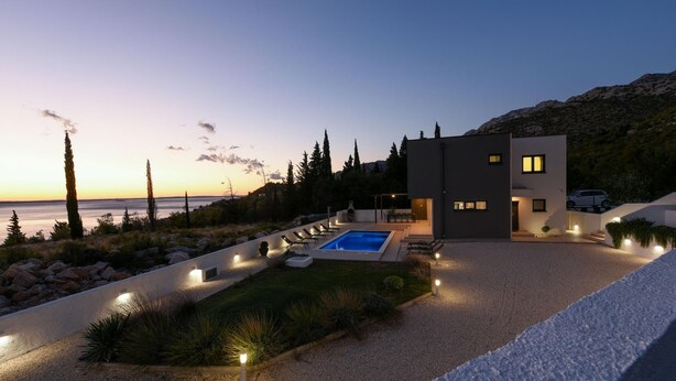A modern house with a swimming pool, a well-maintained garden, and a view of the sea at dusk. - Villa Royal Promons Zadarvillas (Starigrad)