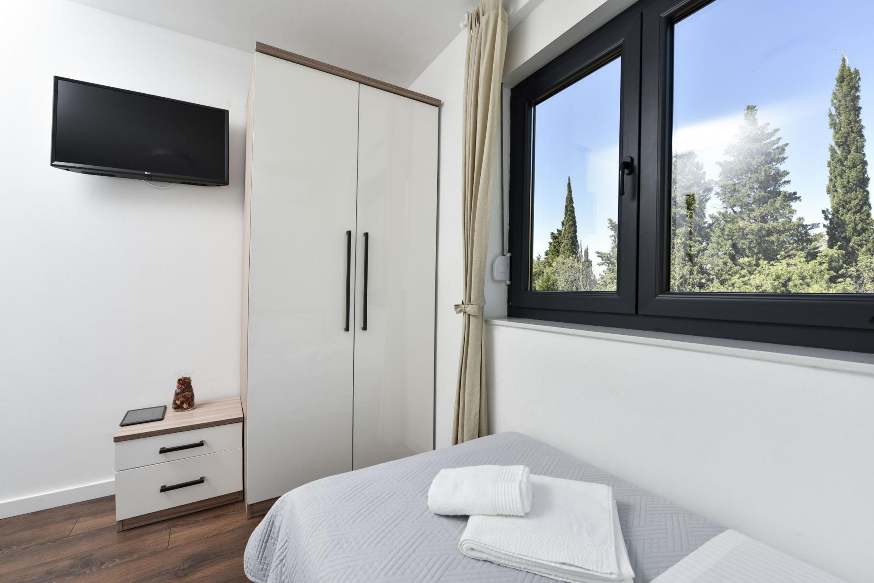 A bedroom with a bed, a bedside table with a tablet, a wardrobe, and a TV mounted on the wall.