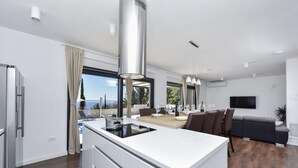 A modern kitchen with a central island, a dining area with a view, and a living space with a sofa and TV. - Villa Royal Promons Zadarvillas (Starigrad)