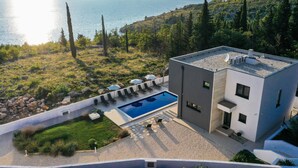 A modern building with a swimming pool, surrounded by greenery and overlooking a body of water. - Villa Royal Promons Zadarvillas (Starigrad)