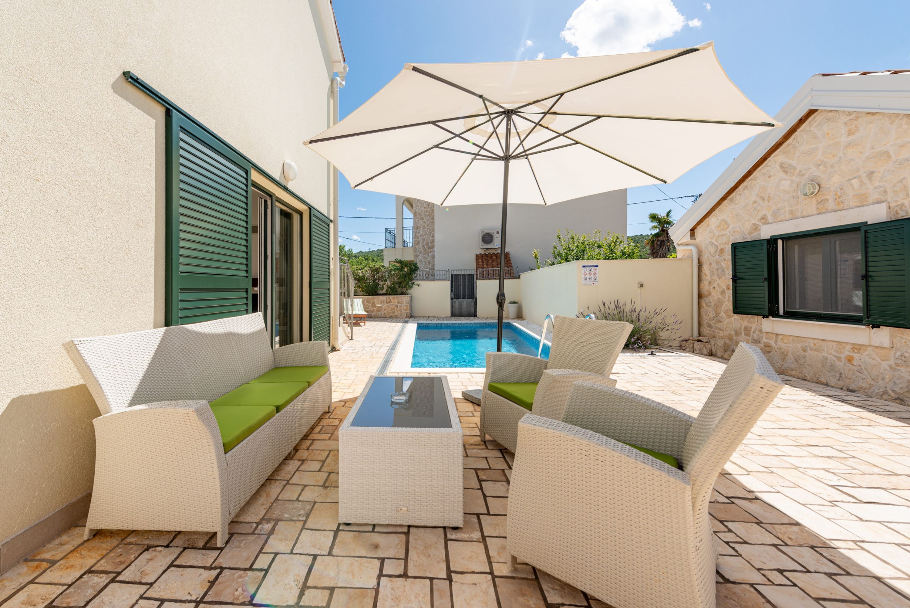 A patio with wicker furniture, a pool, and a stone wall.