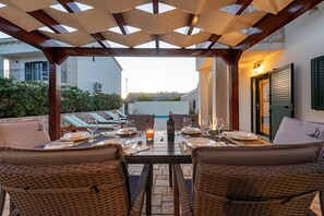 Un espacio de comedor al aire libre con sillas de mimbre y una mesa lista para dos, con vista a un patio y edificios, además de una calle.