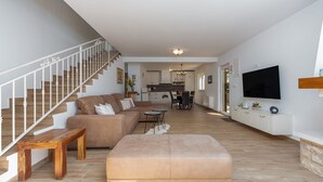 Un vaste espace de vie comprenant un escalier, un canapé, une table basse et un téléviseur fixé au mur.