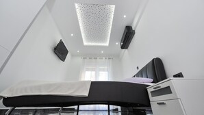 A modern bedroom with a sloped ceiling, a bed, a bedside cabinet, and a window with curtains. - Villa Lily Zadarvillas (Privlaka)