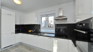 A modern kitchen with white cabinets, a black countertop, and a window providing a view of buildings outside. - Villa Lily Zadarvillas (Privlaka)