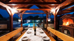 Un espace extérieur aménagé pour les repas, avec une pergola en bois, une piscine et une cheminée en briques.