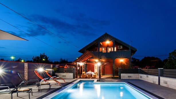 Une maison moderne dotée d’une piscine, d’un espace salon extérieur et d’une terrasse bien éclairée.