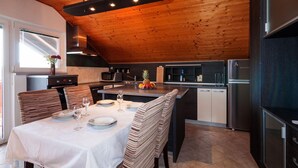 Une cuisine moderne avec un plafond en bois, des appareils en acier inoxydable et un coin repas agrémenté d’une nappe blanche et de chaises à rayures.
