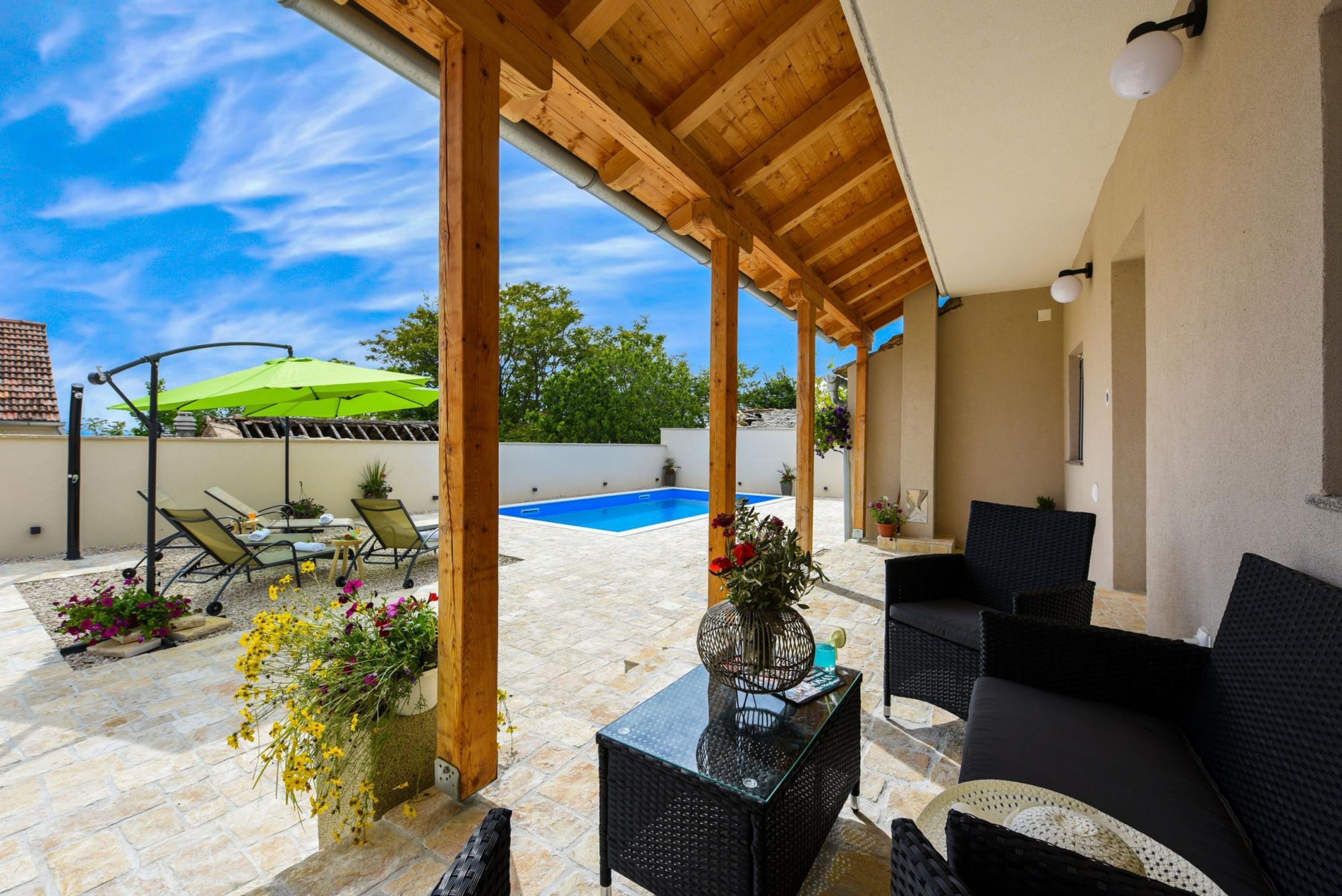 Un patio exterior cubierto con piscina, mobiliario de mimbre y plantas en macetas.