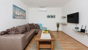 Ein modernes Wohnzimmer mit einem Ecksofa, einem Holztisch, einem Flachbildfernseher und einem an der Wand montierten Regal mit einem Router und Dekorationselementen.
