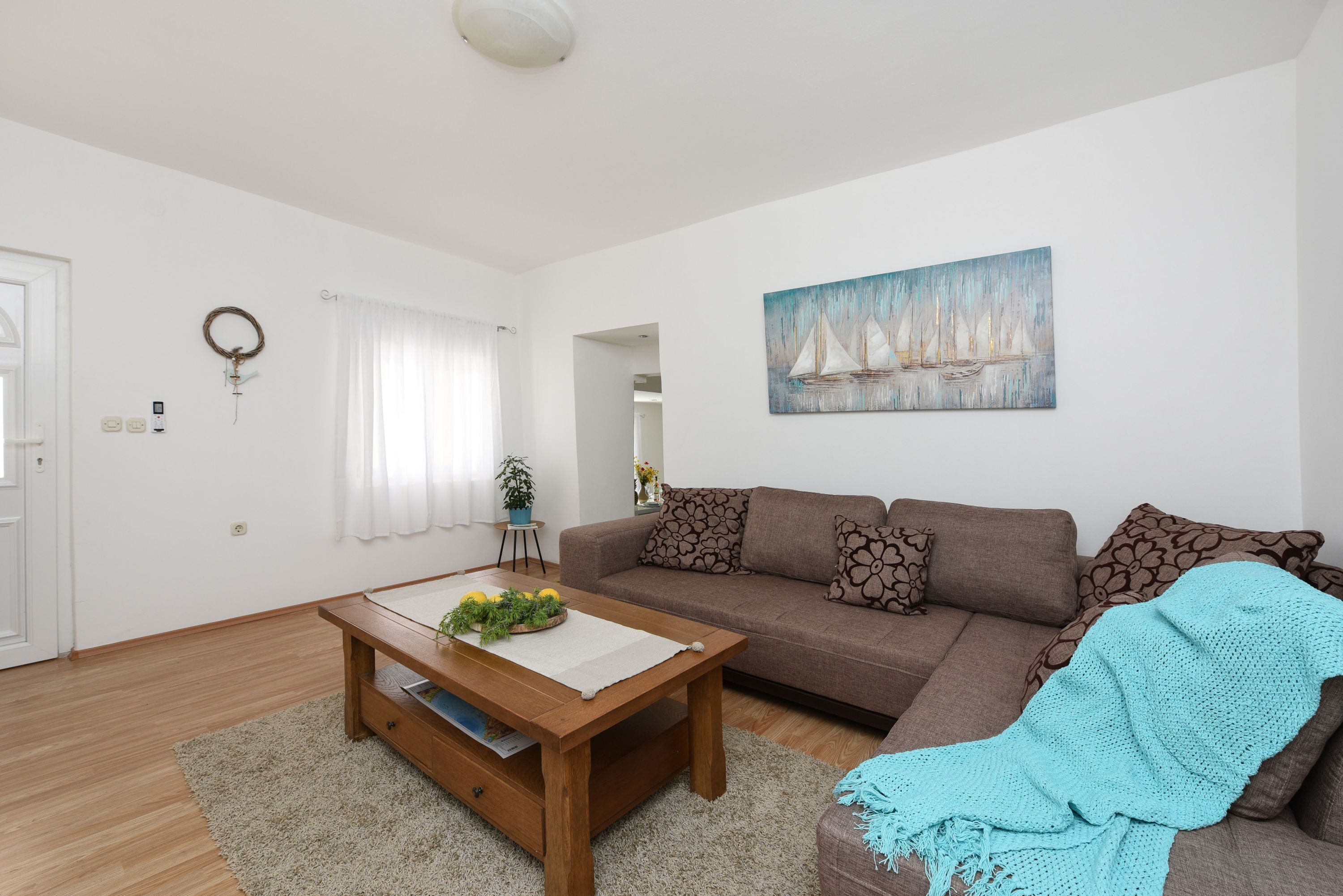 Ein modernes Wohnzimmer mit einem braunen Sofa, einem Couchtisch aus Holz mit einer Pflanze und einem Gemälde von Segelbooten an der Wand.