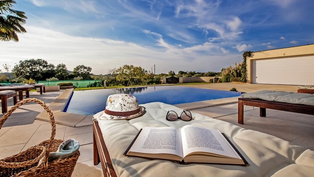 Zona de piscina con una silla de descanso, un sombrero, un libro y un par de gafas.