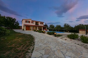 A two-story house with a stone pathway leading to a swimming pool.