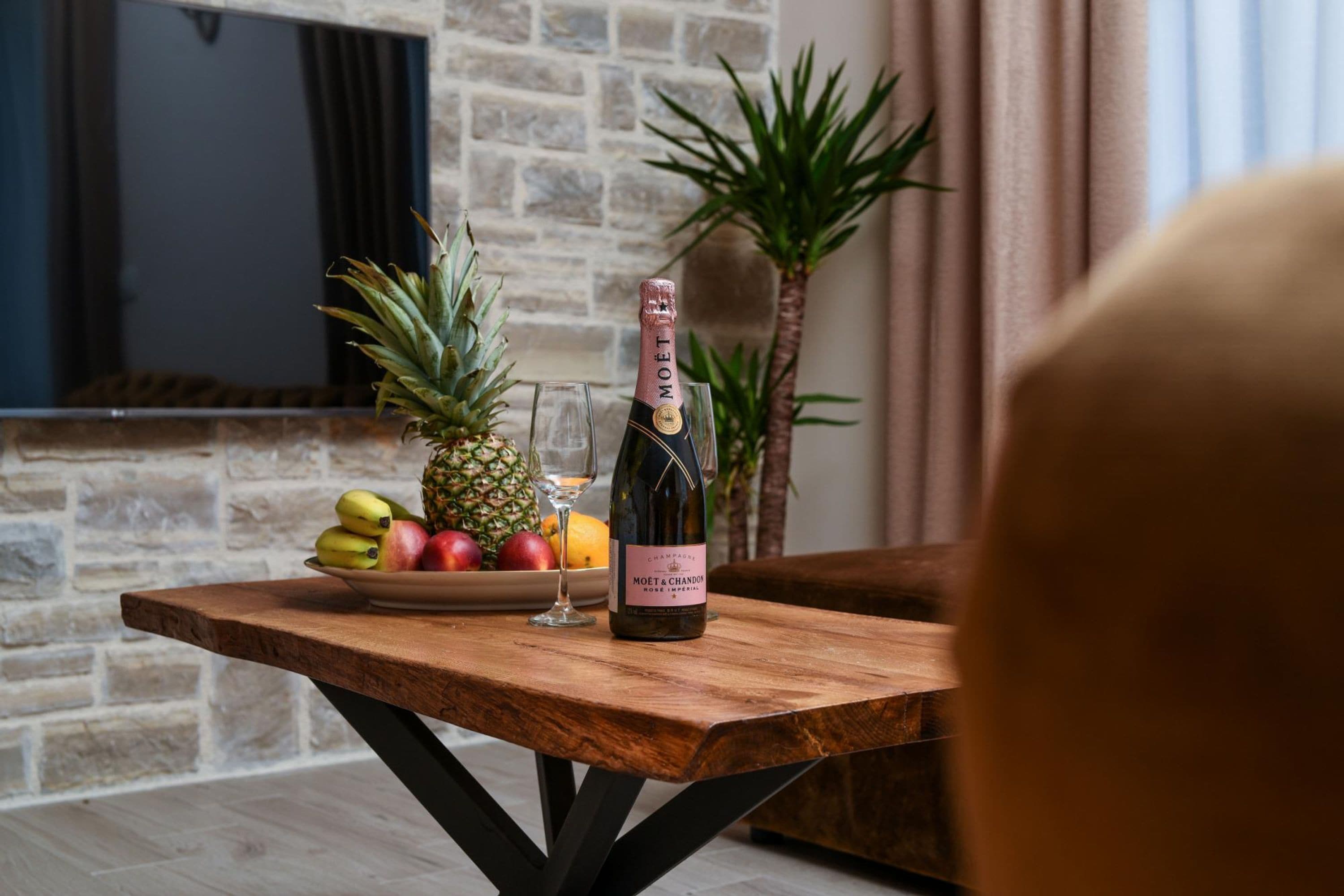 Een houten tafel met een fles champagne, een glas en een schaal fruit.