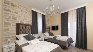 Une chambre d’hôtel avec un mur en pierre, deux lits avec des têtes de lit assorties, un lustre et un téléviseur à écran plat.