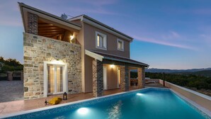 Une maison moderne à deux étages, dotée d’une piscine, d’une façade en pierre et offrant une vue sur les montagnes.