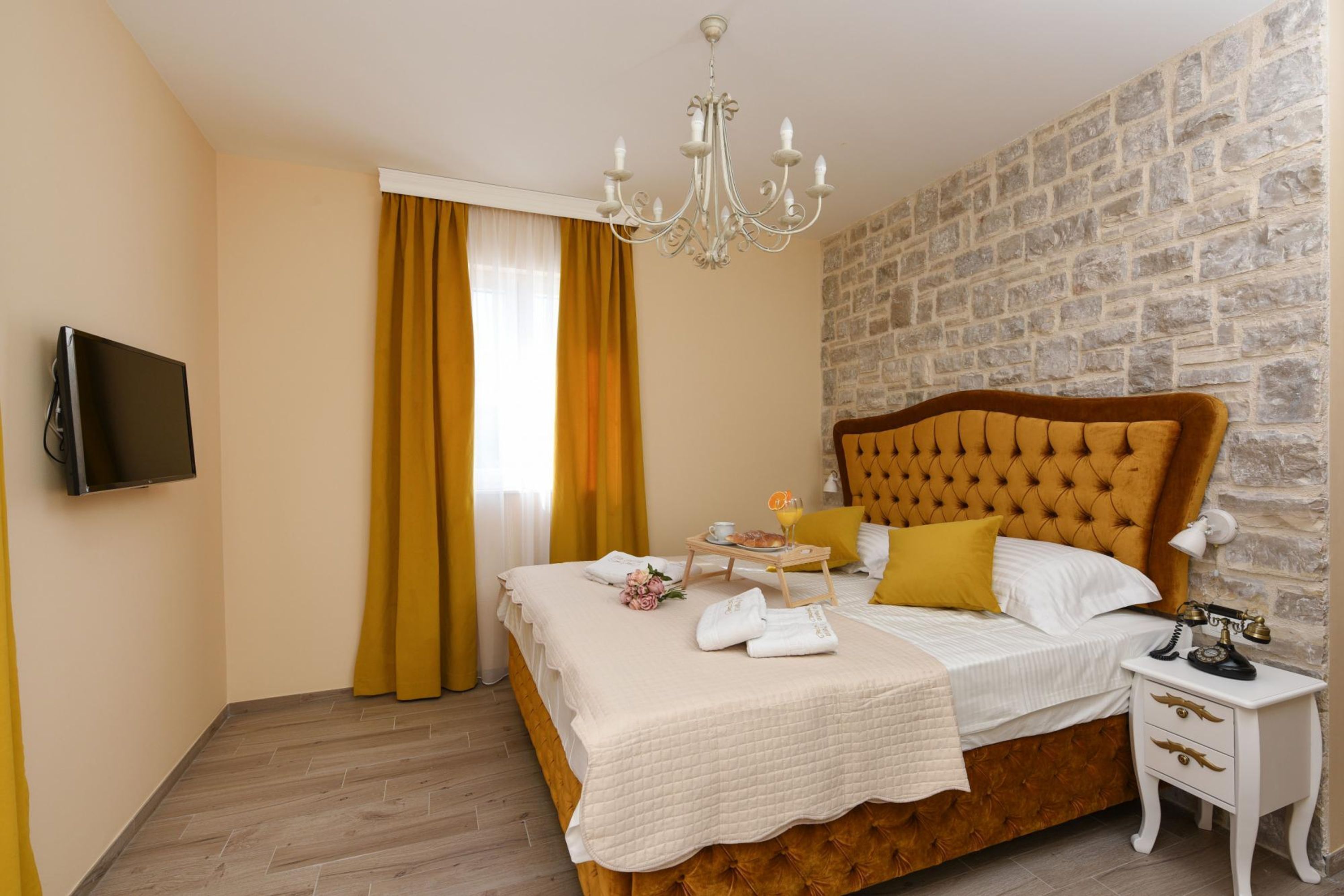 Une chambre d’hôtel avec un lit, une télévision, un lustre, un mur en pierre et un plancher en bois.